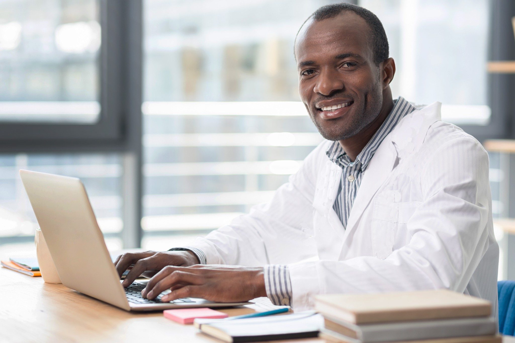 Male scientist in a lab coat smiling while he sits at the computer 