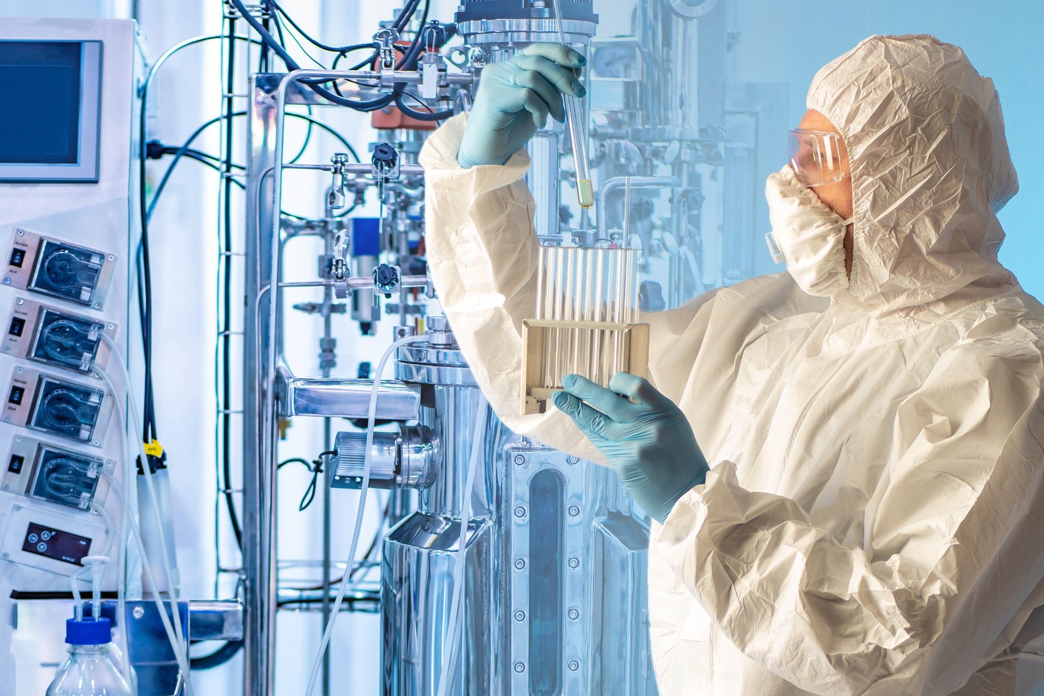 Scientist holding a test tube next to a bioreactor